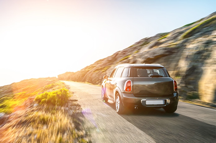 Automóvil avanzando por una carretera junto a un entorno natural rocoso, iluminado por la luz cálida del atardecer