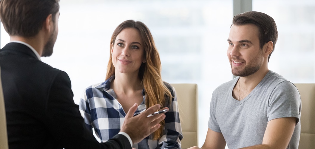 Reunión en una oficina luminosa donde varias personas conversan alrededor de una mesa mientras una de ellas explica un punto con gestos y documentos