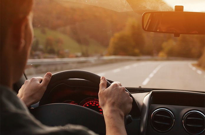 Vista desde el interior de un vehículo, con las manos sujetando el volante mientras el coche avanza por una carretera abierta al atardecer