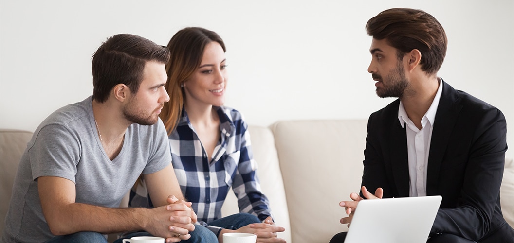 Reunión en un salón, con varias personas sentadas frente a una mesa baja mientras una de ellas utiliza un ordenador portátil para explicar información