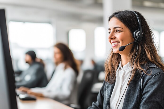 Espacio de oficina con varias personas trabajando frente a ordenadores, utilizando auriculares en un entorno profesional luminoso y organizado