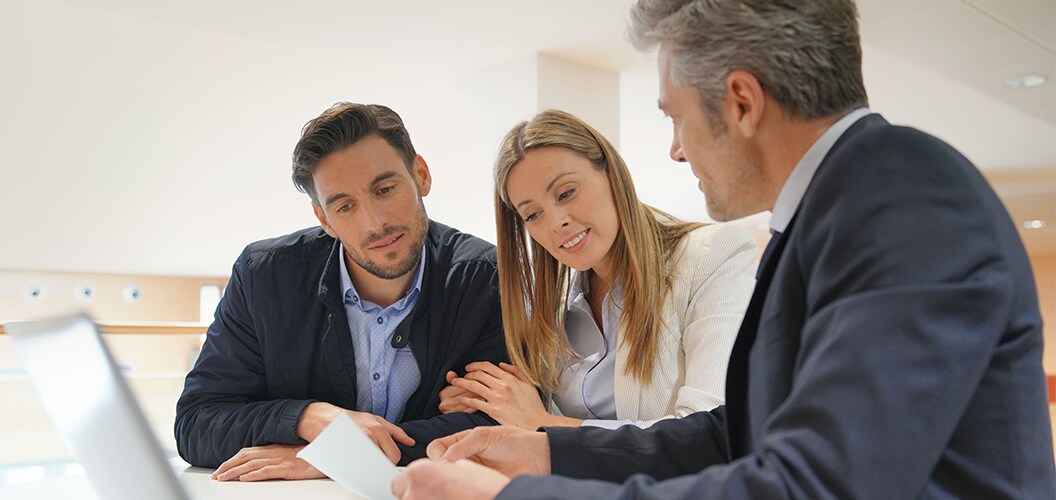 Reunión en un entorno de oficina, con varias personas sentadas alrededor de una mesa mientras revisan documentación y reciben explicaciones durante una consulta