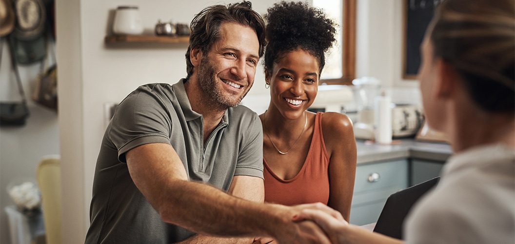 Reunión en una cocina o comedor del hogar, con varias personas estrechando manos tras una conversación junto a una mesa con documentos