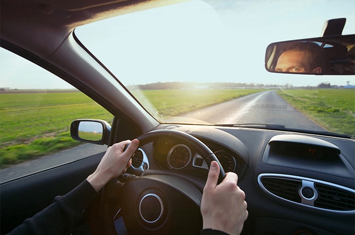 Vista desde el interior de un vehículo, con las manos sujetando el volante mientras se circula por una carretera rural recta y despejada