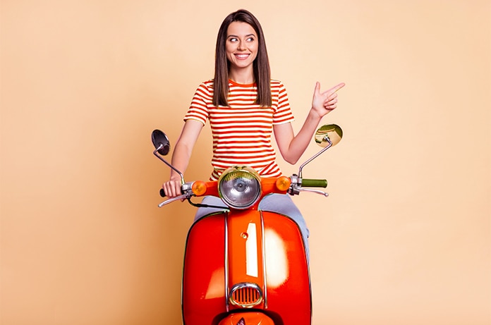 Persona sentada sobre un ciclomotor rojo en un estudio con fondo liso, realizando un gesto de señalización con la mano