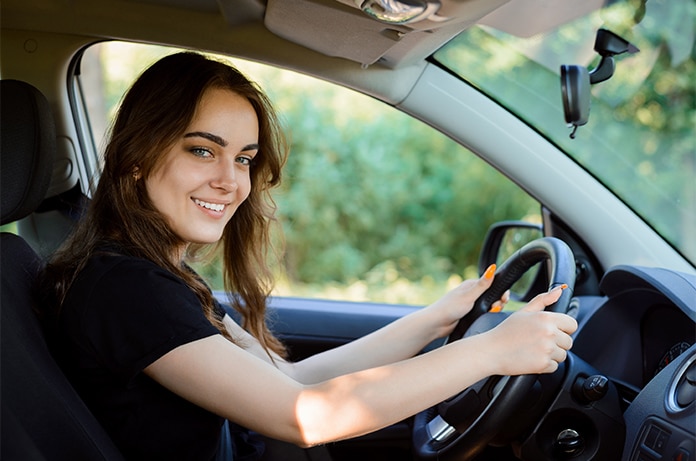 Vista lateral del interior de un vehículo, con una persona al volante circulando por una carretera rodeada de vegetación