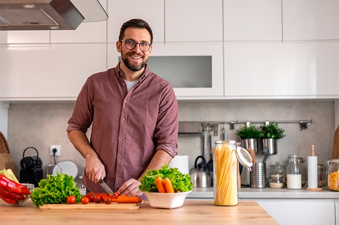 Persona preparando alimentos sobre una encimera de cocina, cortando verduras junto a utensilios y recipientes de cristal