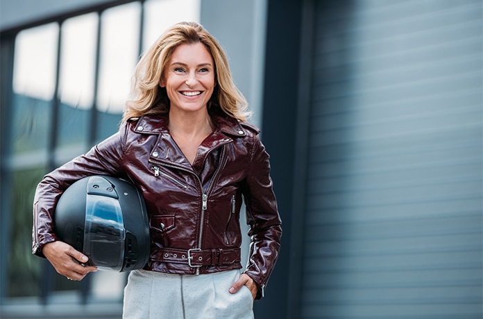 Persona de pie en un entorno urbano moderno, sosteniendo un casco de motocicleta y vistiendo chaqueta de cuero, junto a un edificio de líneas contemporáneas