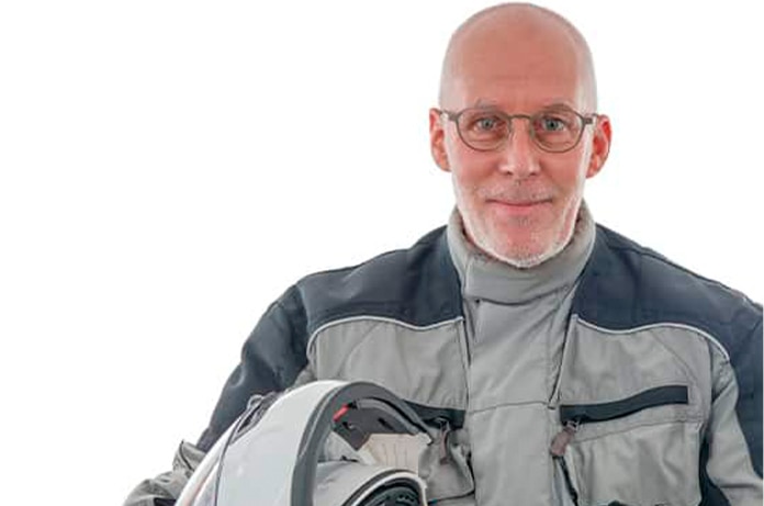 Persona con equipación de motociclista sujetando un casco integral sobre un fondo blanco neutro