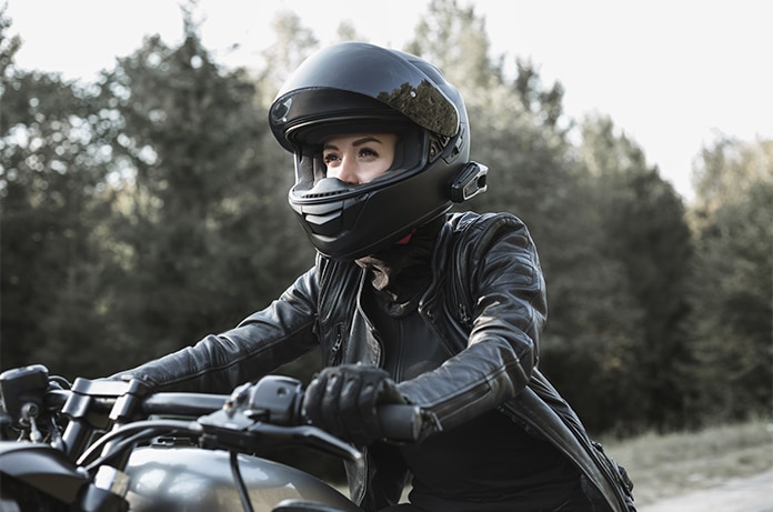 Persona conduciendo una motocicleta por un camino rodeado de árboles, equipada con casco integral y chaqueta de protección