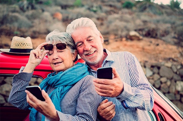 Pareja apoyada en un vehículo rojo descapotable, utilizando teléfonos móviles en un entorno natural y rocoso