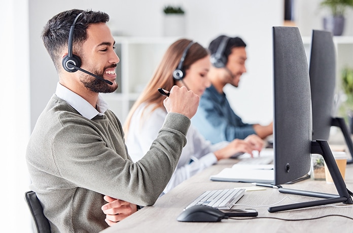 Equipo de atención al cliente trabajando en una oficina moderna, con varias personas utilizando auriculares frente a monitores de ordenador en un entorno luminoso y organizado