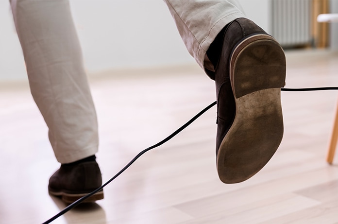 Detalle de un pie levantándose del suelo mientras pisa un cable suelto en el interior de una vivienda, mostrando una situación de posible tropiezo
