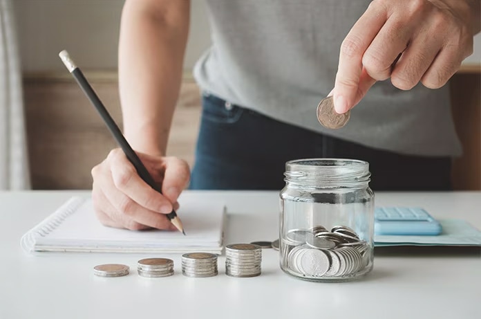 Manos organizando y contando monedas mientras se anotan gastos en una libreta, simbolizando planificación financiera
