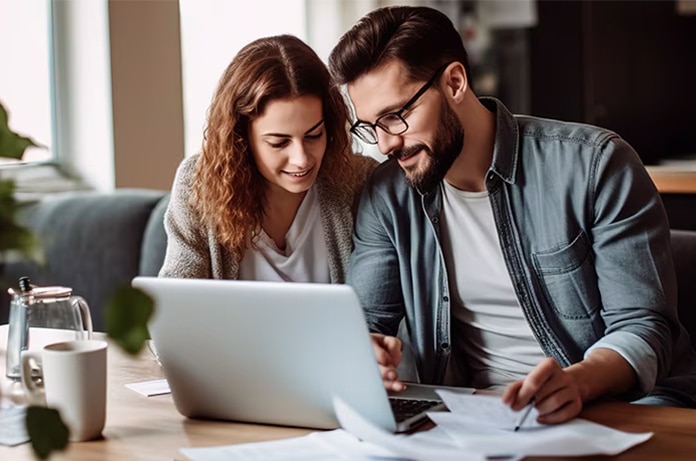 Dos personas revisando documentos y utilizando un ordenador portátil en una mesa de trabajo