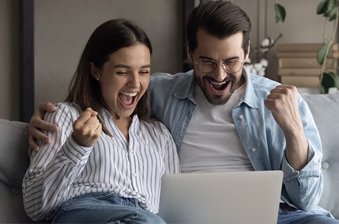 Dos personas sentadas juntas en un sofá celebrando algo mientras miran la pantalla de un portátil