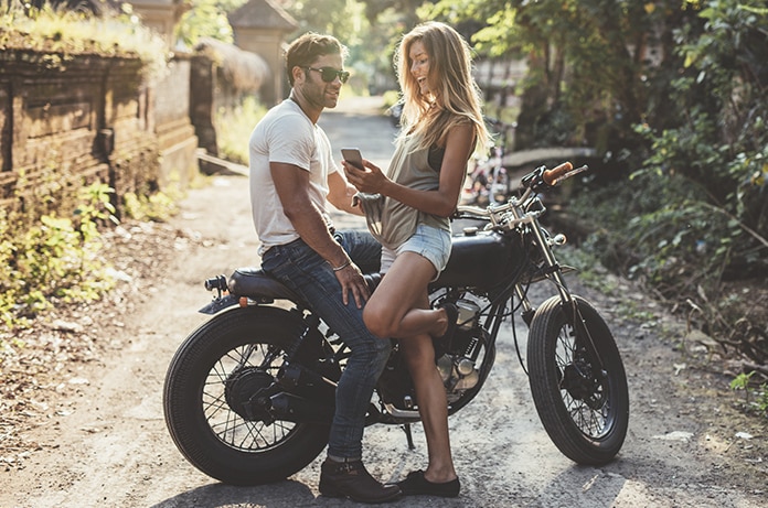 Chica mirando el móvil junto a un chico sobre una moto parado en un camino