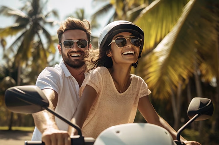 Dos personas en moto avanzando entre palmeras en un entorno tropical iluminado por el sol