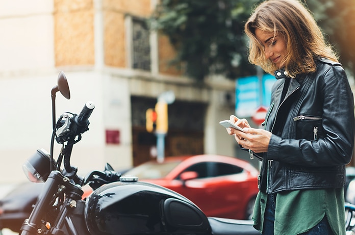 Chica mirando su móvil junto a su motocicleta