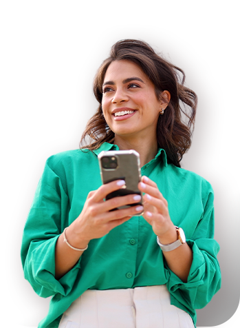 Persona sosteniendo un teléfono móvil con ambas manos sobre un fondo blanco, vistiendo una camisa verde y accesorios visibles en las muñecas