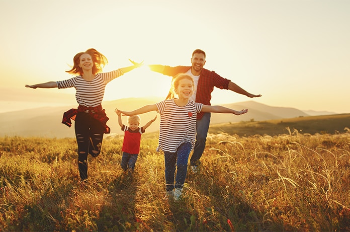 Grupo familiar avanzando por un campo al atardecer con los brazos extendidos mientras caminan entre la hierba
