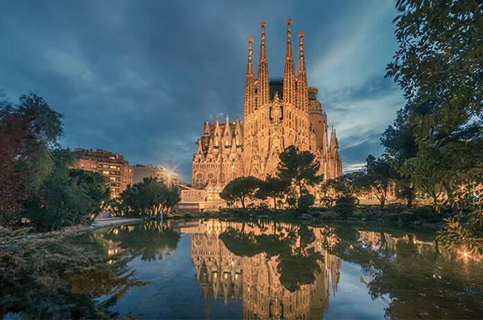 Basílica de la Sagrada Familia iluminada al atardecer reflejada en un estanque rodeado de árboles