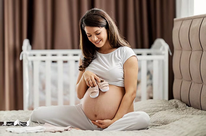 Persona embarazada sosteniendo su barriga y posando unas zapatillas de prenatal sobre su tripa