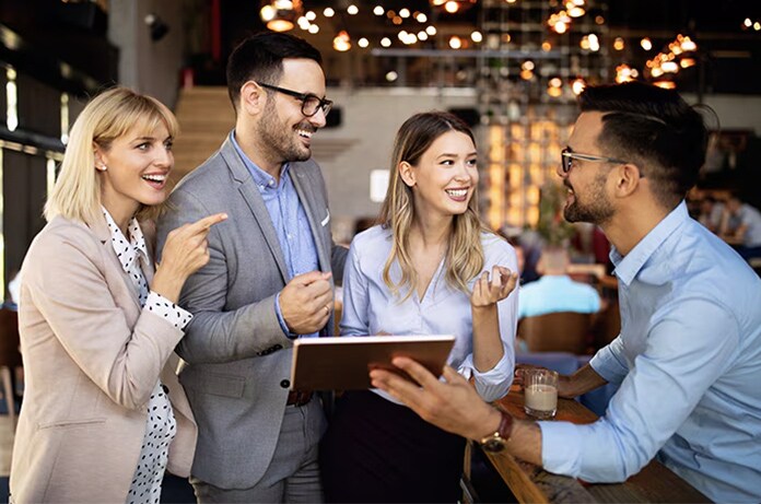 Grupo de personas conversando en un entorno laboral relajado mientras revisan información en una tableta sobre una barra alta