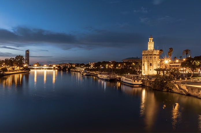 Vista nocturna del paseo fluvial de Sevilla iluminado, con la Torre del Oro a la derecha