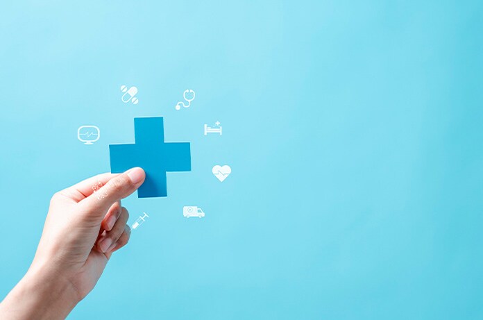 Mano sosteniendo una cruz azul rodeada de pequeños iconos relacionados con servicios sanitarios