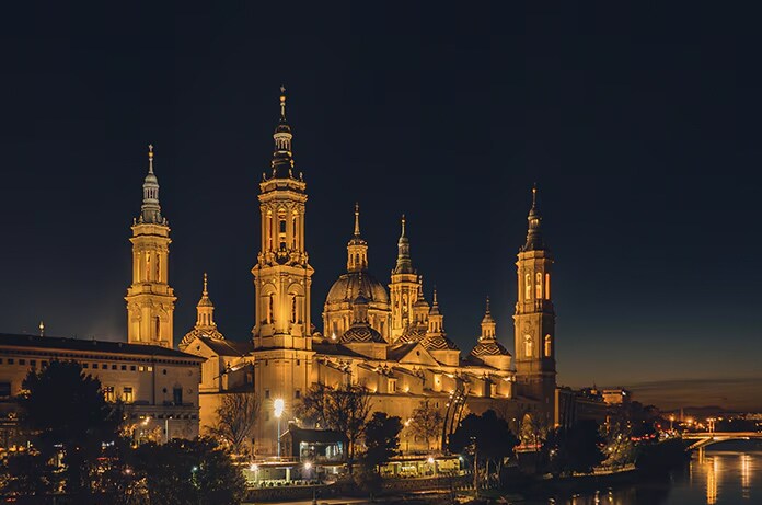 Basílica de Zaragoza iluminada al anochecer destacando su arquitectura sobre el fondo oscuro del cielo