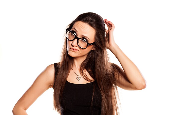 Persona con el cabello largo sujetando la cabeza con una mano mientras luce un colgante en forma de corazón sobre un fondo claro