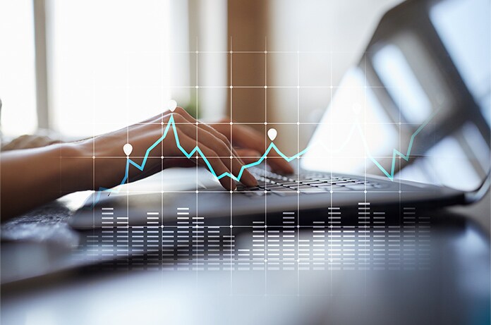 Manos tecleando en un ordenador portátil con gráficos superpuestos que muestran líneas de evolución y barras de datos