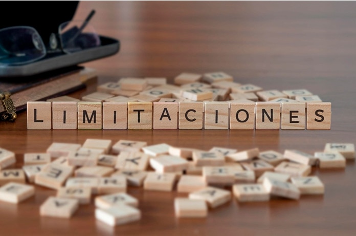 Letras de madera colocadas sobre una mesa formando la palabra “LIMITACIONES”, rodeadas de otras piezas dispersas con caracteres impresos