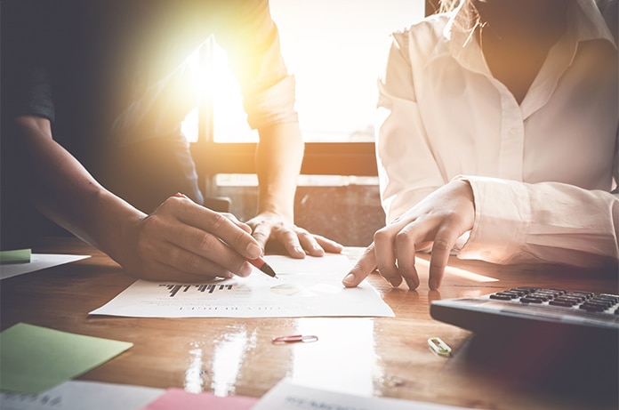 Varias manos señalando y revisando documentos con gráficos impresos en una mesa iluminada por luz natural