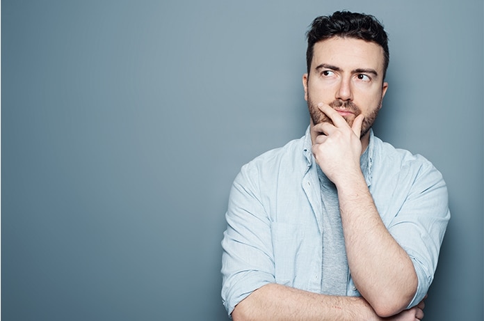 Persona con camisa clara posando con una mano apoyada bajo la barbilla sobre un fondo liso de color gris