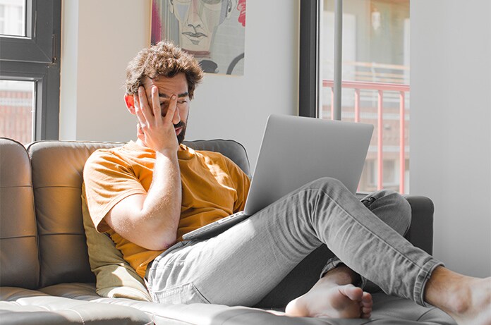 Persona sentada en un sofá utilizando un ordenador portátil en un espacio interior iluminado por la luz natural