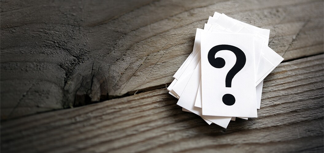 Montón de tarjetas blancas sobre una superficie de madera, con un gran signo de interrogación impreso en la tarjeta superior