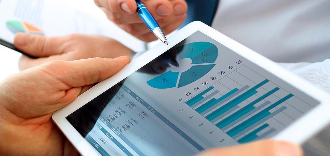 Dispositivo digital mostrando gráficos circulares y de barras mientras una mano señala los datos con un bolígrafo