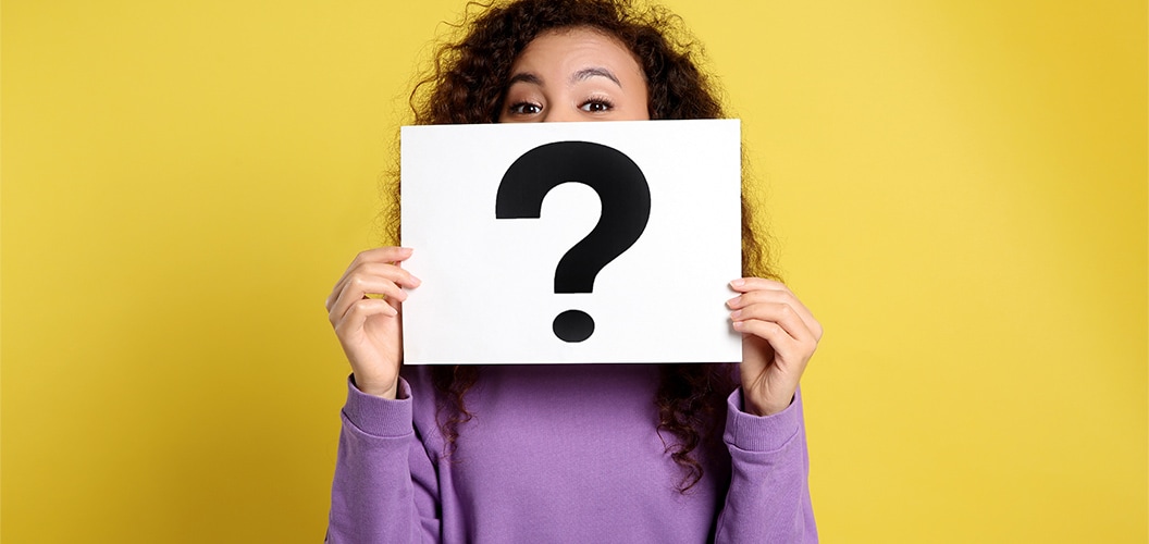 Persona con sudadera morada sosteniendo una cartulina con un gran signo de interrogación sobre un fondo amarillo