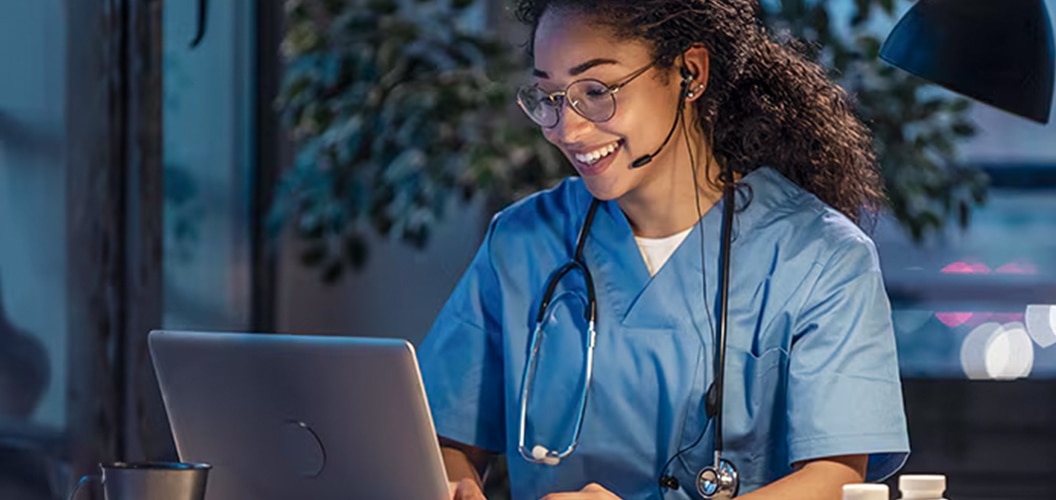 Persona con indumentaria sanitaria utilizando un ordenador portátil en un entorno interior con iluminación tenue y material clínico sobre la mesa