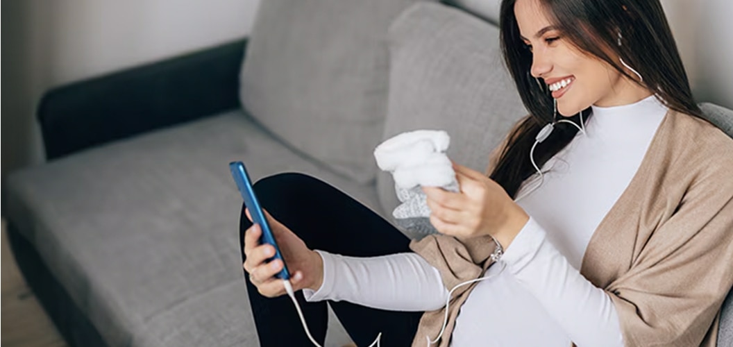 Persona embarazada realizando una videollamada desde un sofá enseñando unos patucos a la persona al otro lado del teléfono