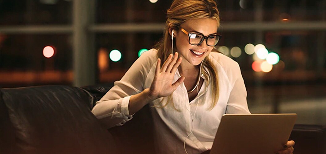 Persona saludando a través de una videollamada desde un sofá, utilizando una tableta con auriculares conectados