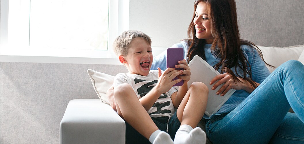 Persona adulta y menor sobre un sofá riendo mientras miran un móvil