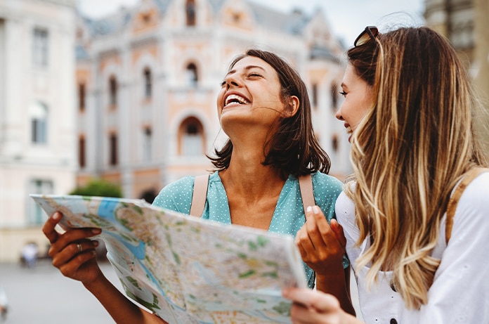 Dos personas consultando un mapa en una plaza urbana, con edificios históricos de fachada ornamentada al fondo